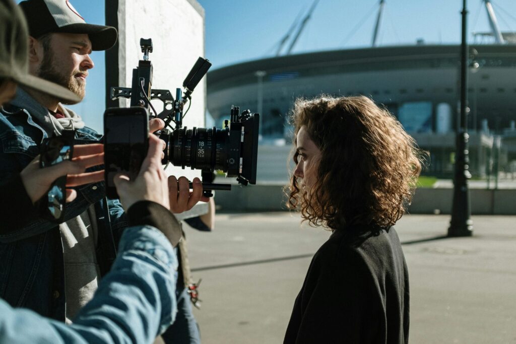 Professional filmmakers capturing a scene outdoors near a stadium, featuring equipment and creative process.
