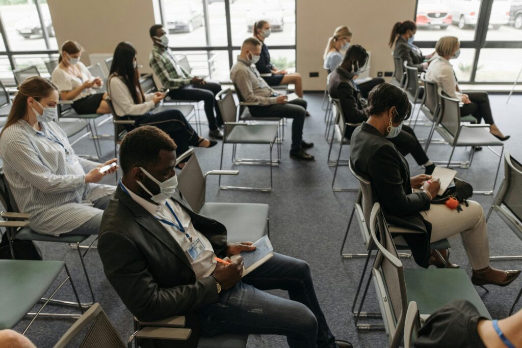 Business seminar with diverse attendees wearing masks, maintaining social distance indoors.
