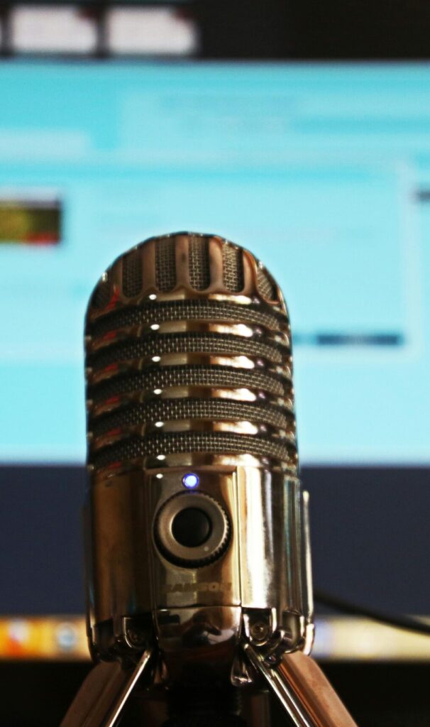 Close-up of a microphone with a blurred computer screen in the background, ideal for podcast themes.