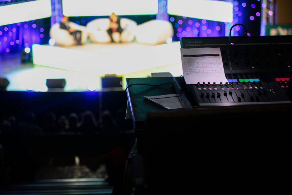 Sound console in a studio setting for a live event with blurred audience view.