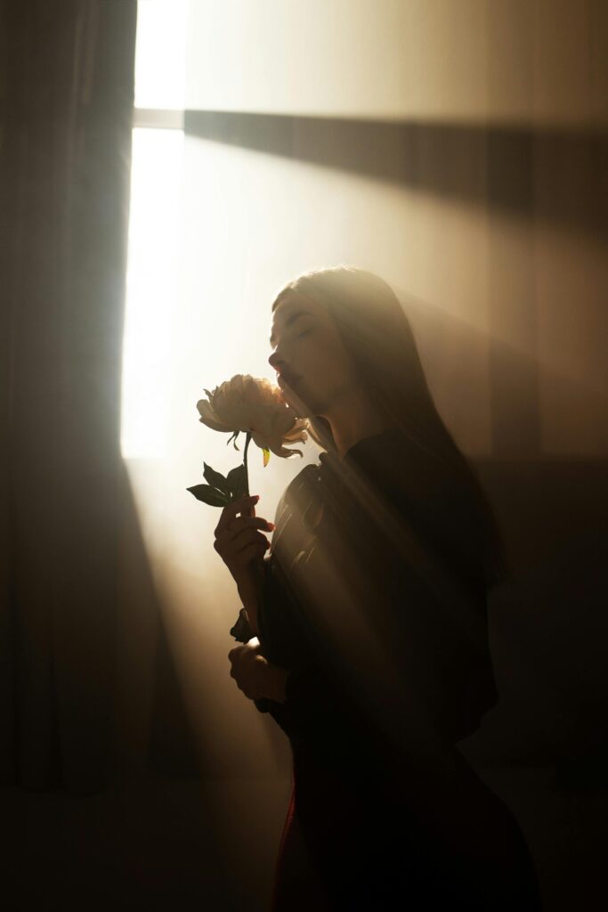 Artistic silhouette of a woman holding a flower in a sunlit room, creating a warm and moody atmosphere.