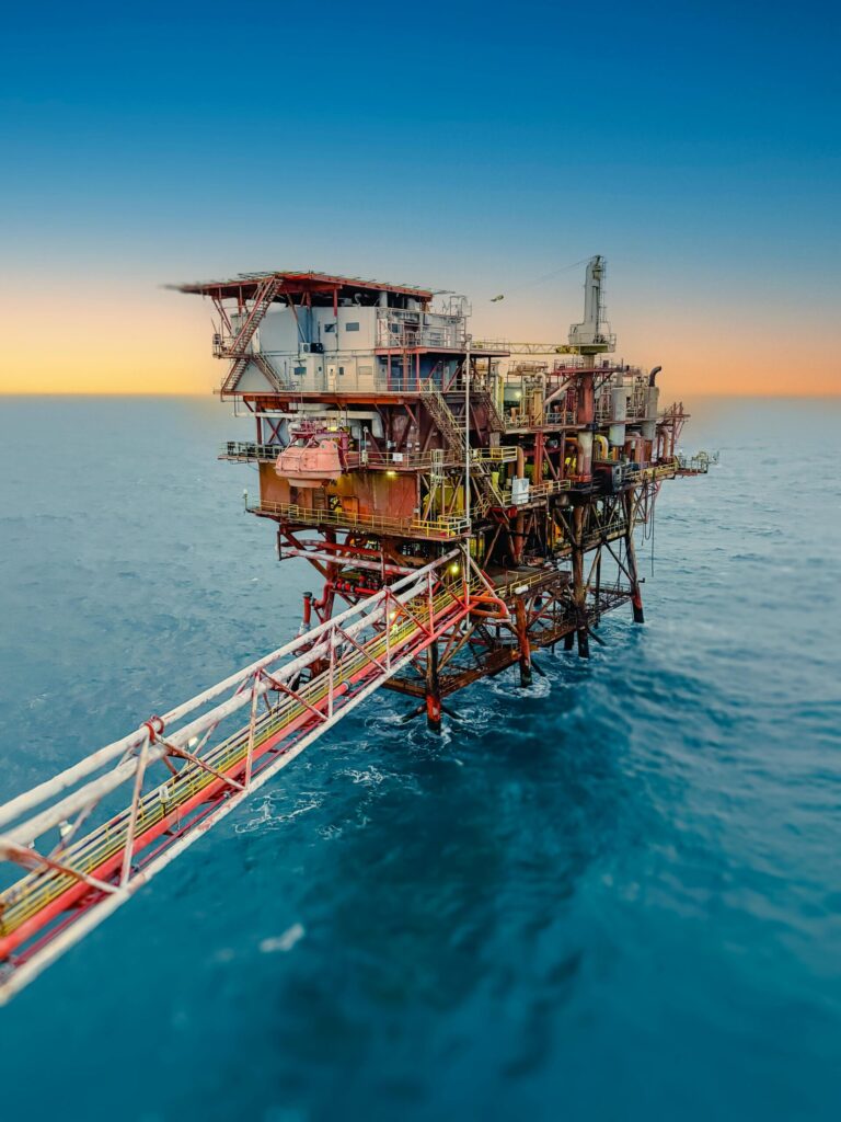 Aerial view of an offshore oil rig surrounded by the ocean at sunset, under a clear sky.